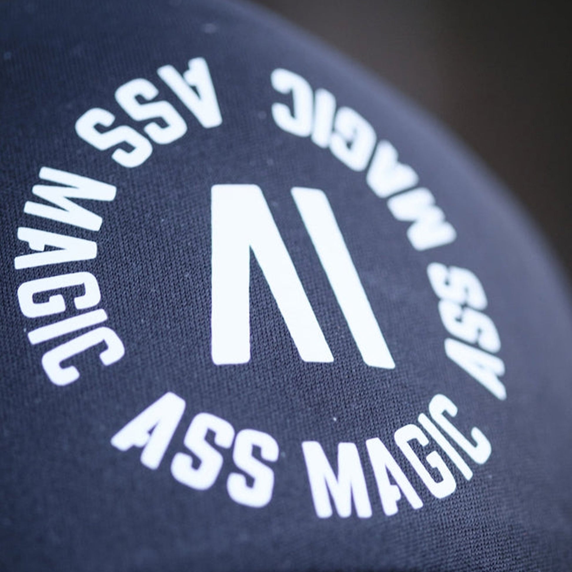 Truckerkeps med närbild av vit Ass Magic-text på mörkt tyg
