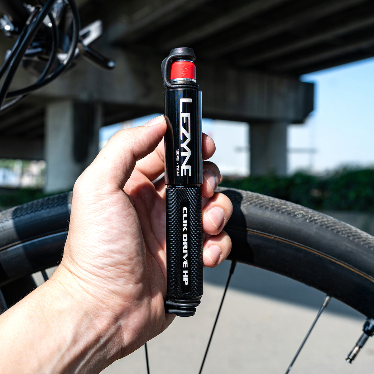 Hand som håller Lezyne handpump, svart grepp och röd ventilkåpa på cykeldäck