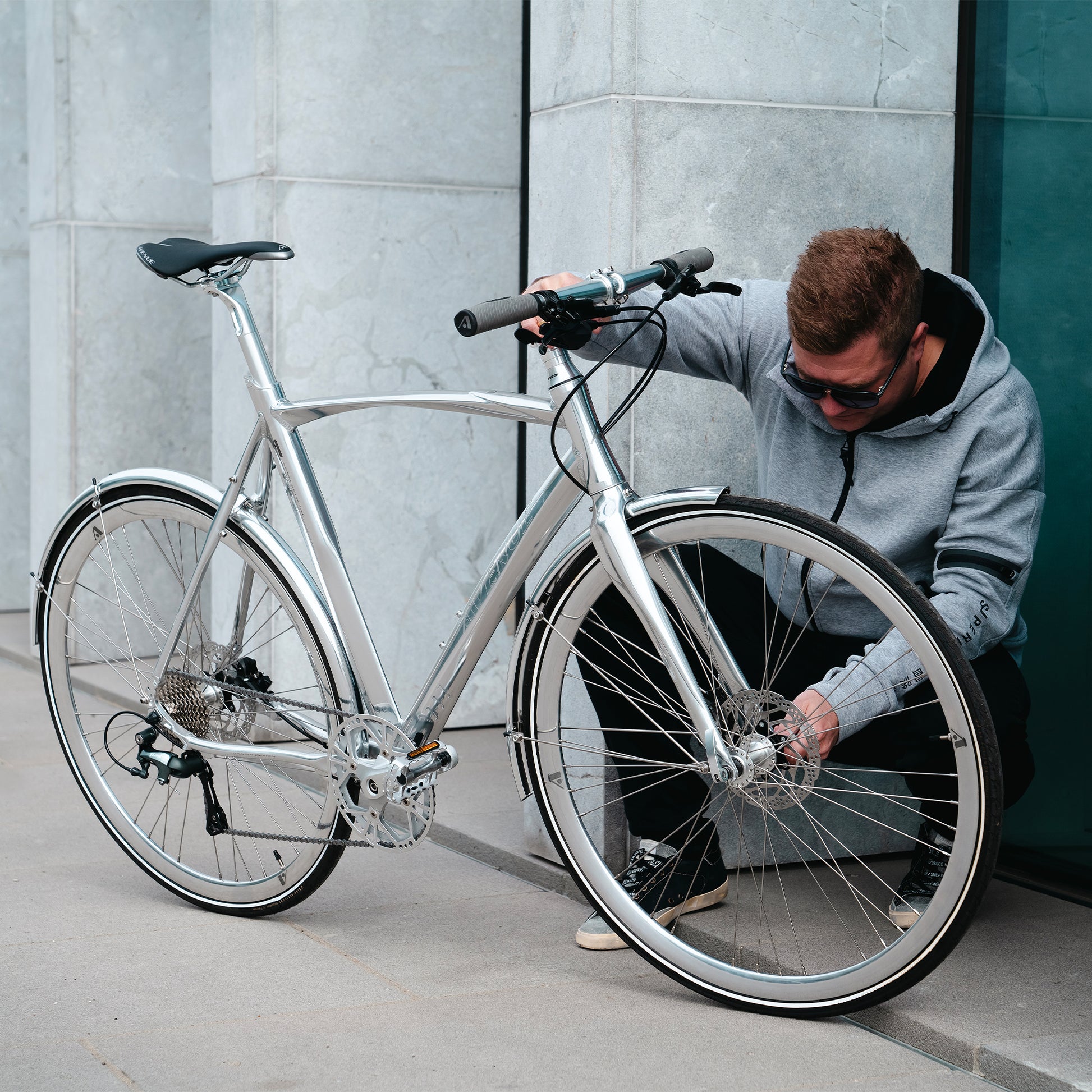 Metallcykel i blank silver med framhjul och styre, användare vid cykeln